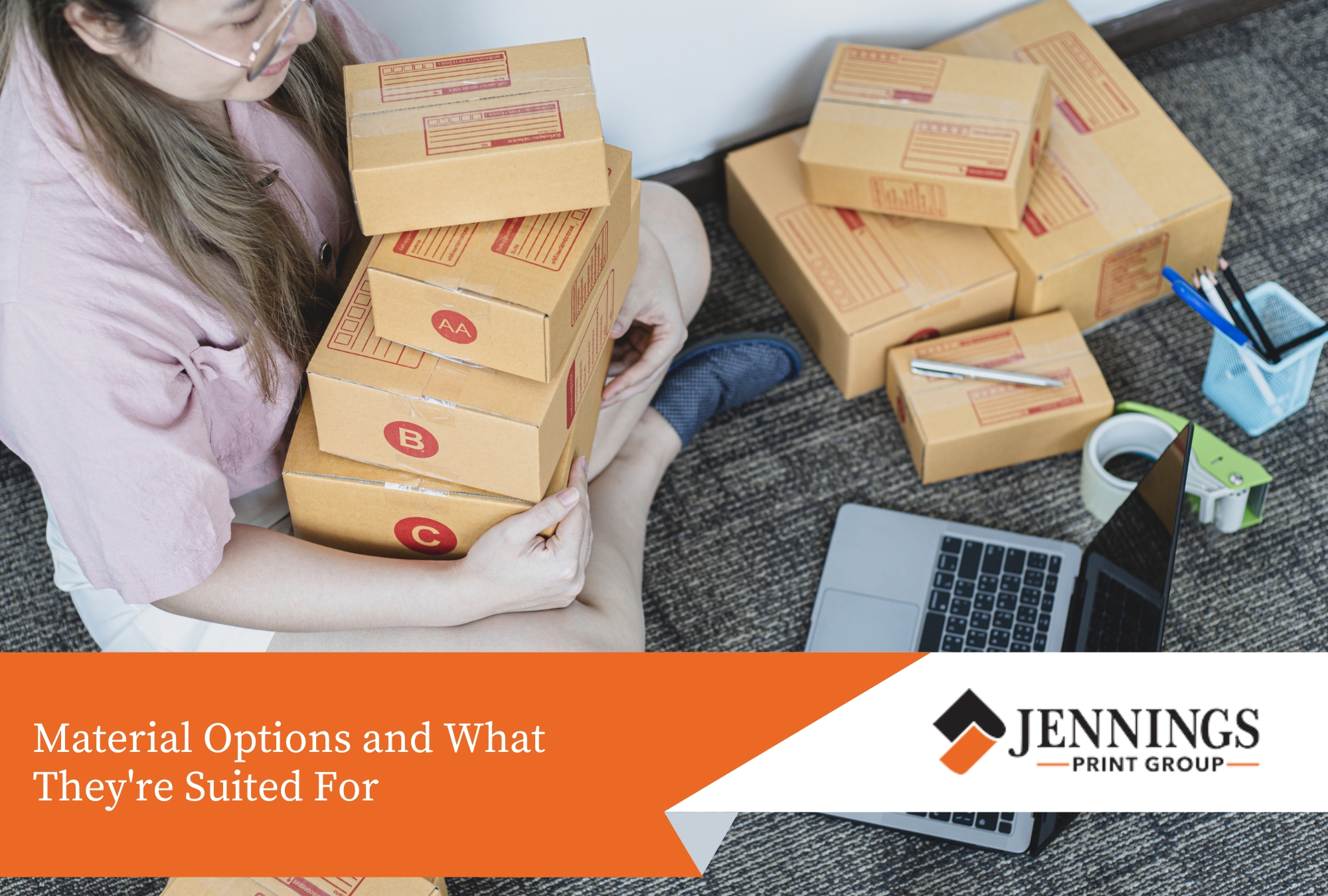 Custom Packaging: What Small Businesses Need to Know Before Their First Print Run - custom packaging A person sitting cross-legged on a carpeted floor, holding a stack of small cardboard boxes, next to an open laptop and shipping supplies.